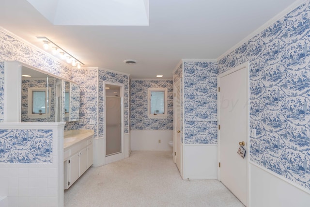 bathroom featuring toilet, vanity, wainscoting, a shower stall, and wallpapered walls