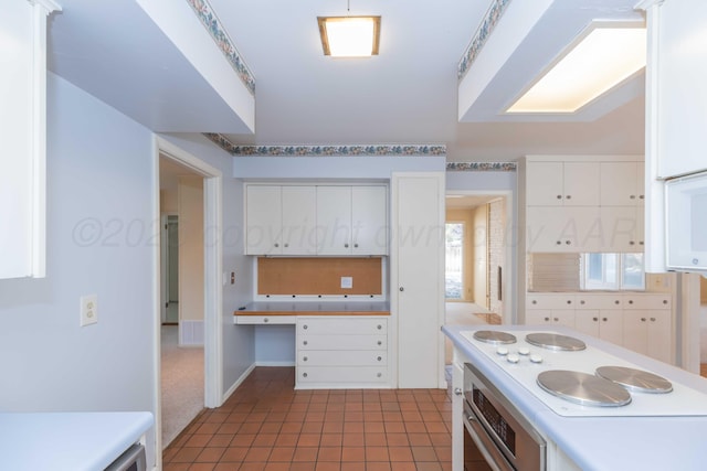 kitchen with oven, dark tile patterned flooring, white cabinets, light countertops, and built in study area