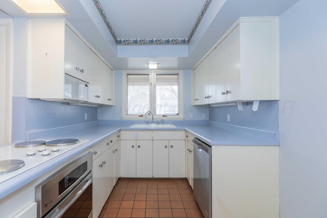 kitchen with white cabinets, appliances with stainless steel finishes, light countertops, dark tile patterned floors, and a sink