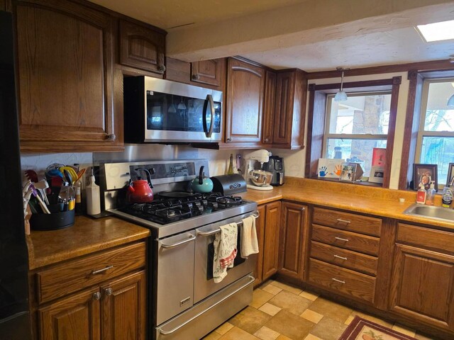 830 Burnett St, Miami, TX 79059 - kitchen featuring hanging light fixtures, a sink, brown cabinets, and appliances with stainless steel finishes