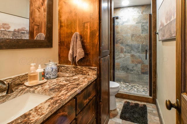 bathroom with toilet, vanity, baseboards, a shower stall, and stone finish floor