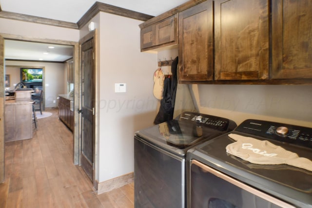 laundry area featuring cabinet space, light wood finished floors, baseboards, crown molding, and washing machine and dryer