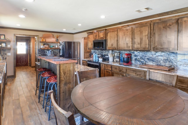 kitchen with a kitchen island, ornamental molding, appliances with stainless steel finishes, light wood-type flooring, and tasteful backsplash