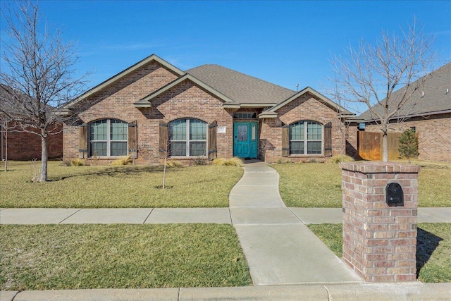 view of front of house with a shingled roof, a front lawn, and brick siding