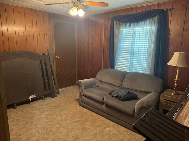 living room featuring light carpet, a ceiling fan, and wooden walls