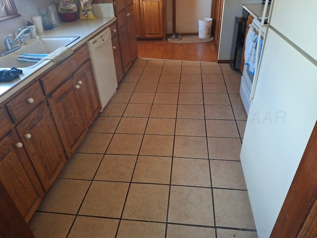 kitchen featuring brown cabinets, light countertops, light tile patterned flooring, a sink, and white appliances