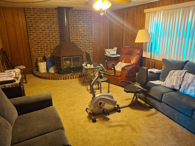 living room with carpet floors, a wood stove, ceiling fan, and wooden walls