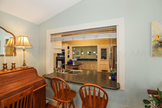 kitchen featuring stainless steel refrigerator, sink, kitchen peninsula, lofted ceiling, and a kitchen bar