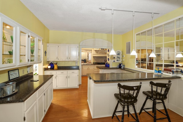 kitchen with track lighting, a kitchen breakfast bar, hanging light fixtures, kitchen peninsula, and white cabinetry