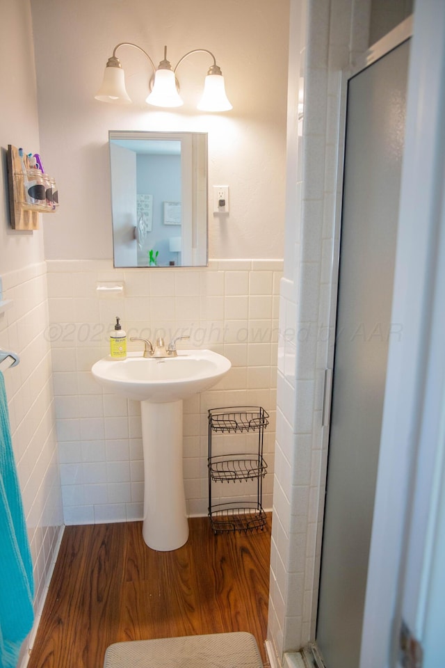 bathroom with a shower stall, wainscoting, wood finished floors, and tile walls