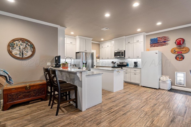 kitchen with a breakfast bar, white cabinetry, stainless steel appliances, light stone countertops, and light hardwood / wood-style floors