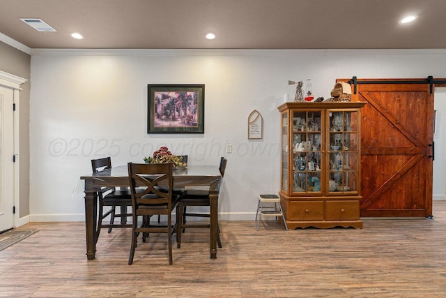 dining room with crown molding, a barn door, and light wood-type flooring