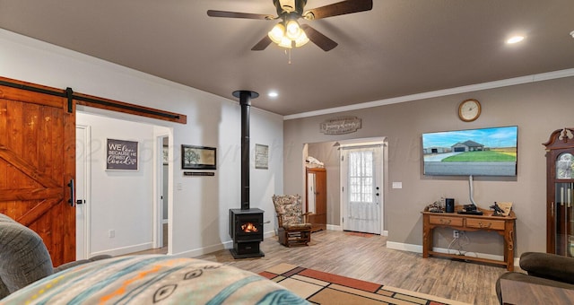 bedroom with crown molding, a barn door, a wood stove, and light wood-type flooring