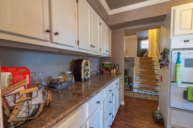 kitchen with ornamental molding, dark stone countertops, double oven, white cabinets, and dark wood-type flooring