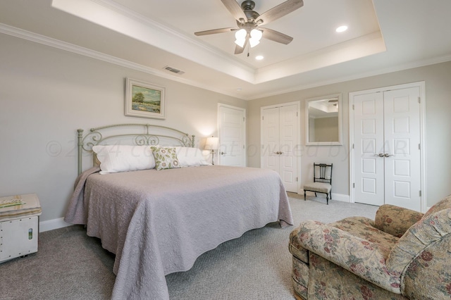 bedroom with a raised ceiling, ceiling fan, light carpet, and two closets