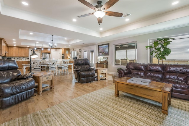 living room with ceiling fan with notable chandelier, light hardwood / wood-style floors, a raised ceiling, and crown molding