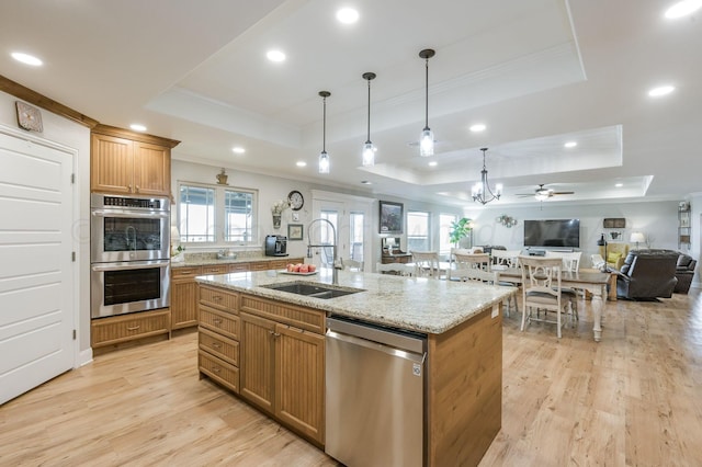 kitchen featuring sink, stainless steel appliances, light hardwood / wood-style flooring, a tray ceiling, and a kitchen island with sink