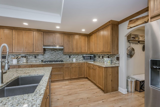 kitchen featuring sink, ornamental molding, light hardwood / wood-style floors, light stone counters, and stainless steel appliances