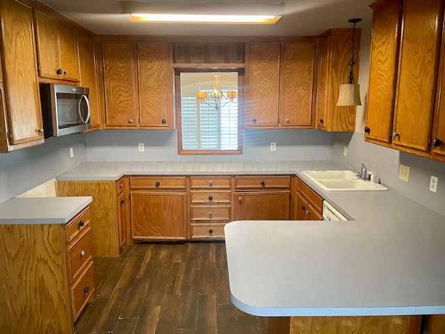 kitchen with kitchen peninsula, dark wood-type flooring, sink, pendant lighting, and a chandelier