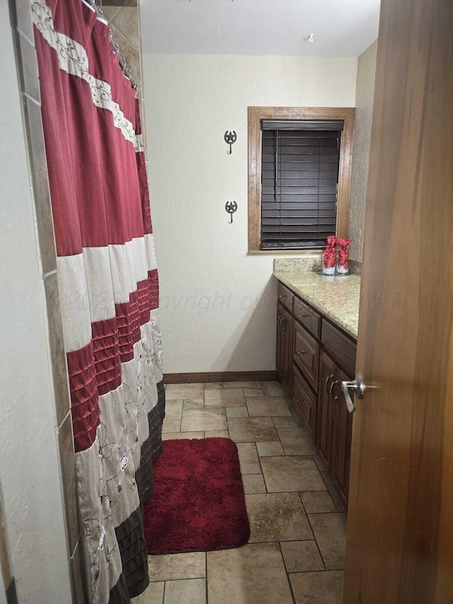 bathroom featuring curtained shower, baseboards, vanity, and stone finish flooring