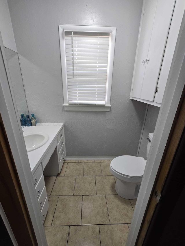 bathroom with baseboards, toilet, a textured wall, tile patterned floors, and vanity