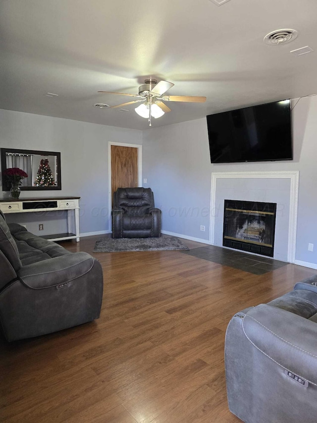 living room featuring visible vents, baseboards, ceiling fan, a fireplace, and wood finished floors