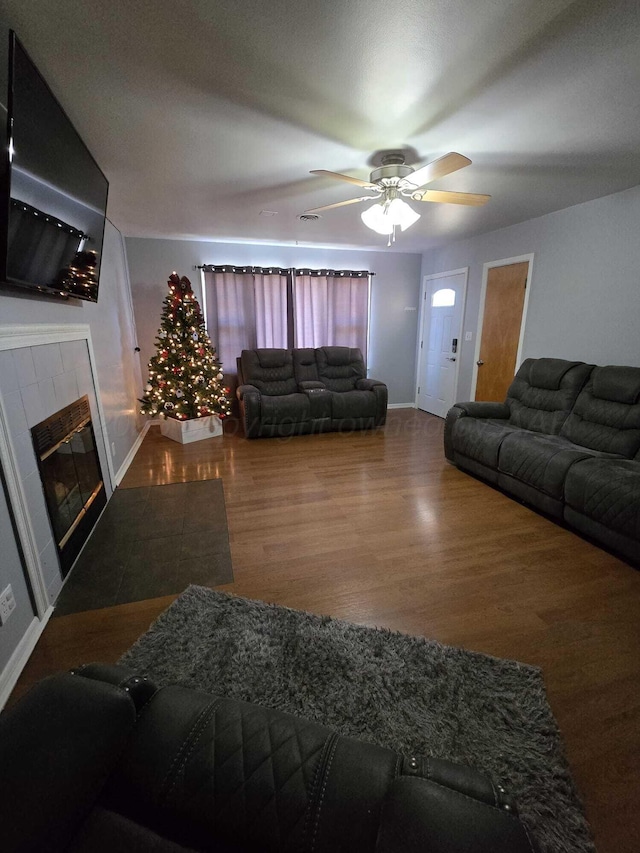 living room featuring a tiled fireplace, wood finished floors, a ceiling fan, and baseboards