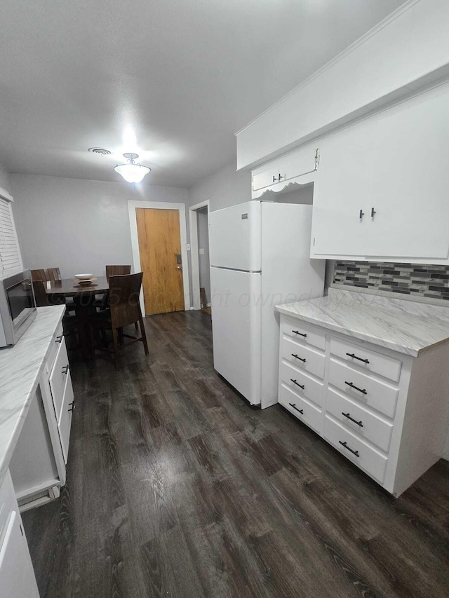 kitchen with stainless steel microwave, backsplash, freestanding refrigerator, white cabinetry, and dark wood-style flooring