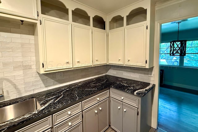 kitchen featuring a sink, decorative backsplash, white cabinets, and dark stone counters