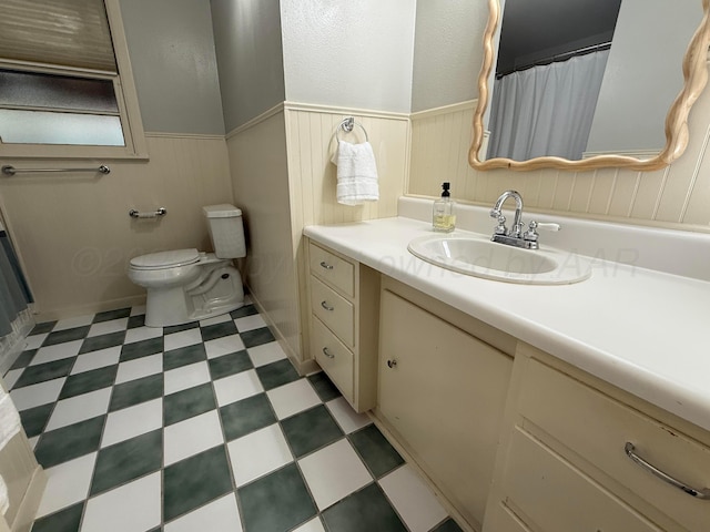 full bath featuring toilet, vanity, curtained shower, tile patterned floors, and wainscoting