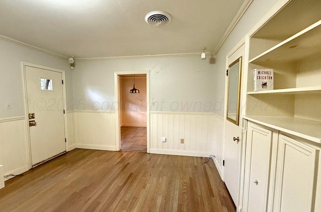 empty room featuring a wainscoted wall, light wood-type flooring, visible vents, and ornamental molding