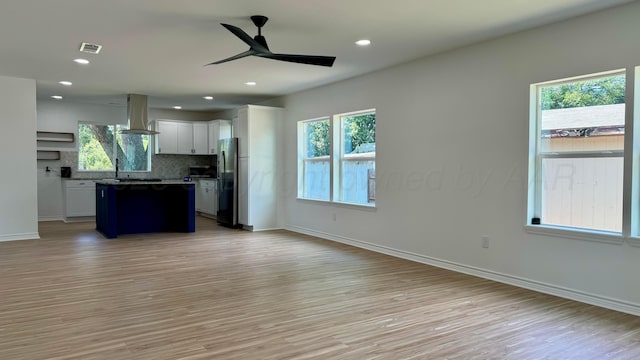 kitchen with stainless steel fridge, white cabinetry, backsplash, a kitchen island, and exhaust hood