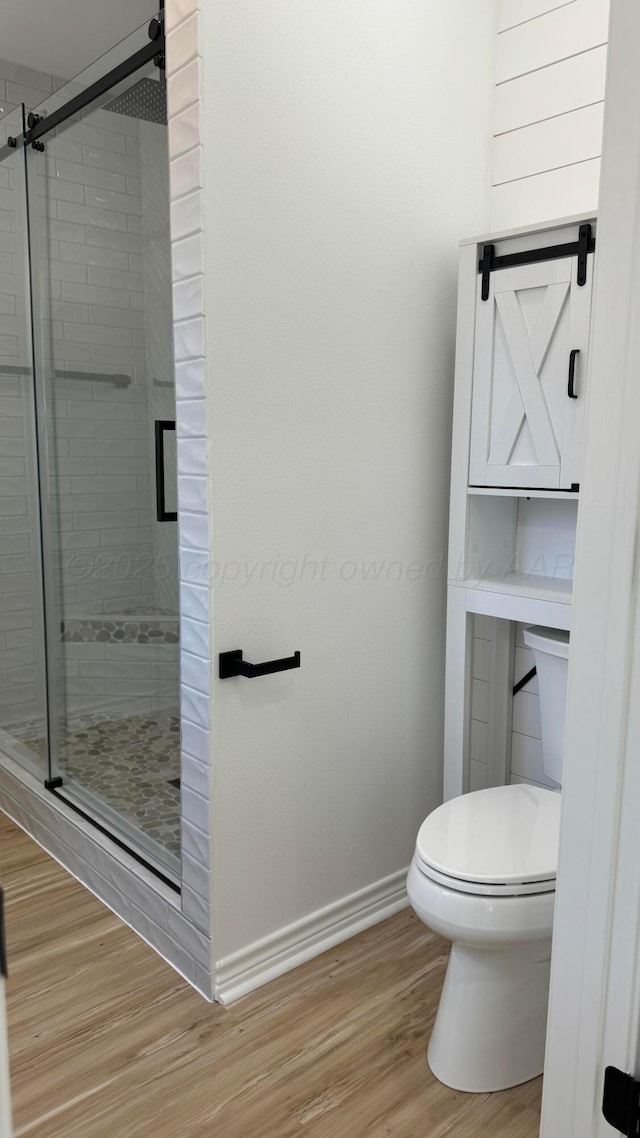 bathroom with a shower with door, hardwood / wood-style floors, and toilet