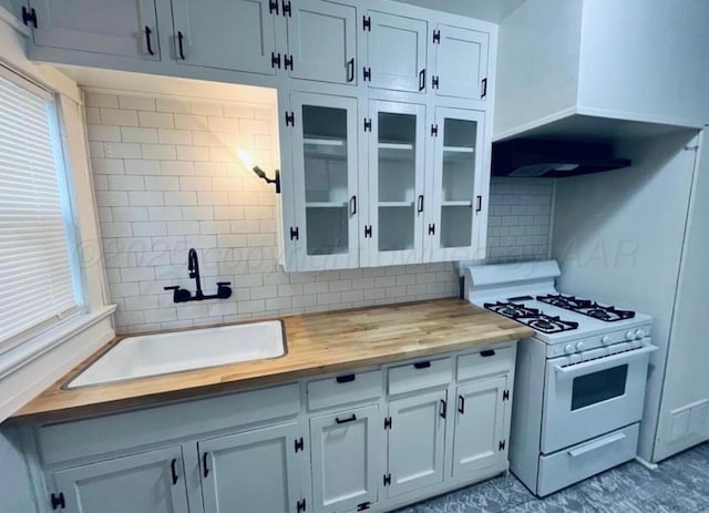 kitchen with white gas range oven, a sink, wooden counters, backsplash, and glass insert cabinets