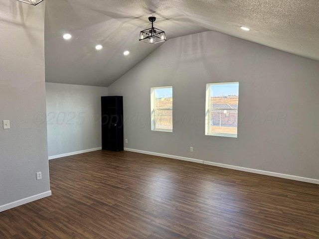 additional living space with a chandelier, a textured ceiling, lofted ceiling, baseboards, and dark wood-style floors