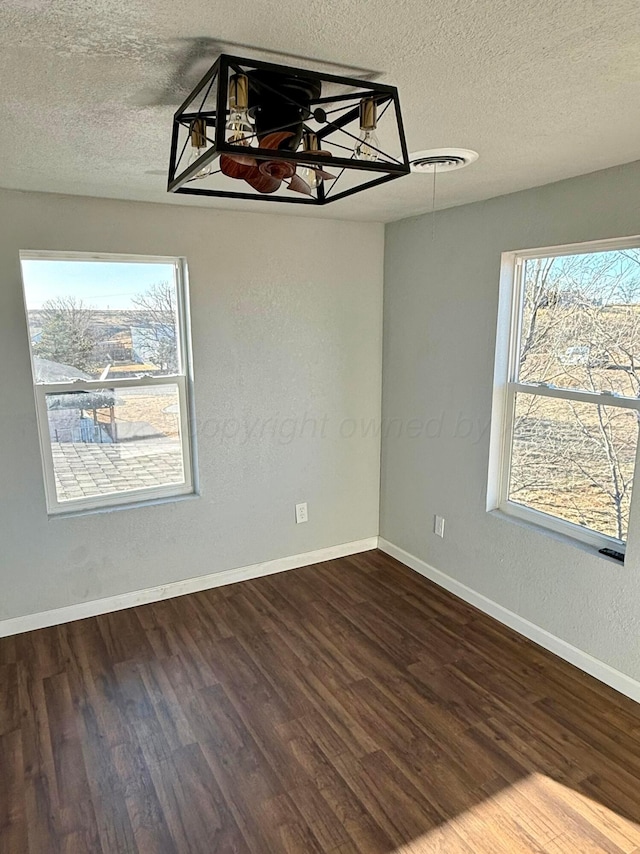 unfurnished room with a textured ceiling, dark wood finished floors, and baseboards