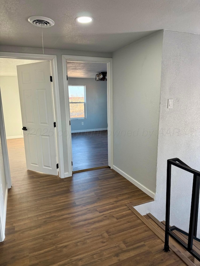 corridor featuring baseboards, visible vents, dark wood-style flooring, a textured ceiling, and recessed lighting