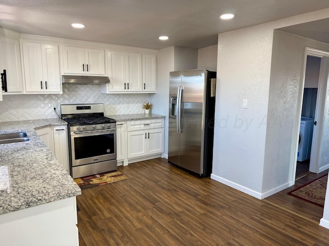 kitchen with under cabinet range hood, white cabinetry, appliances with stainless steel finishes, light stone countertops, and dark wood-style floors