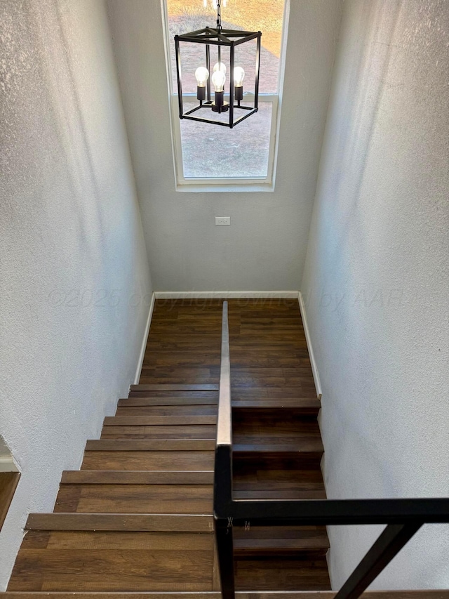 stairs with an inviting chandelier, baseboards, and wood finished floors