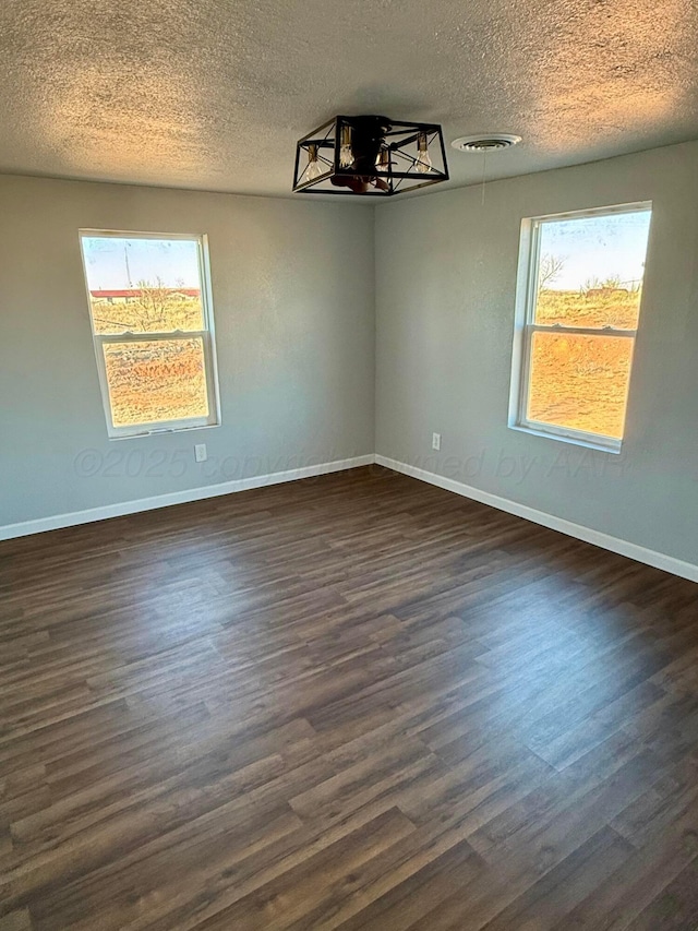 unfurnished room with a healthy amount of sunlight, dark wood-style flooring, visible vents, and baseboards