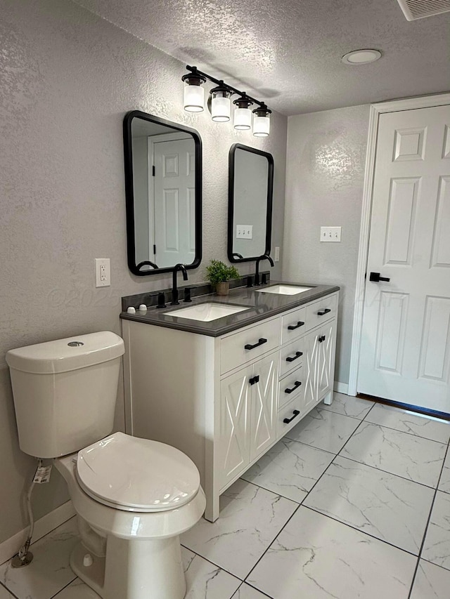 bathroom featuring a textured wall, marble finish floor, a sink, and a textured ceiling