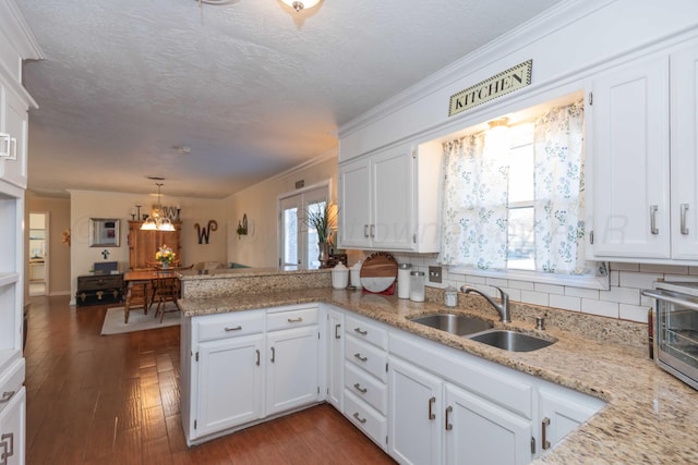 kitchen featuring a peninsula, a sink, dark wood finished floors, and white cabinetry