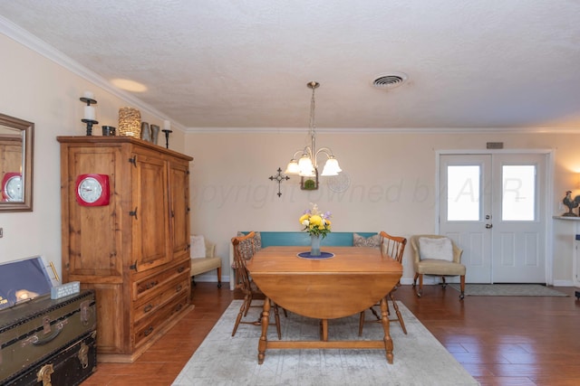 dining space with visible vents, ornamental molding, wood finished floors, a textured ceiling, and a notable chandelier