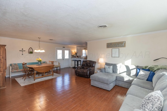 living room featuring a textured ceiling, wood finished floors, visible vents, ornamental molding, and an inviting chandelier