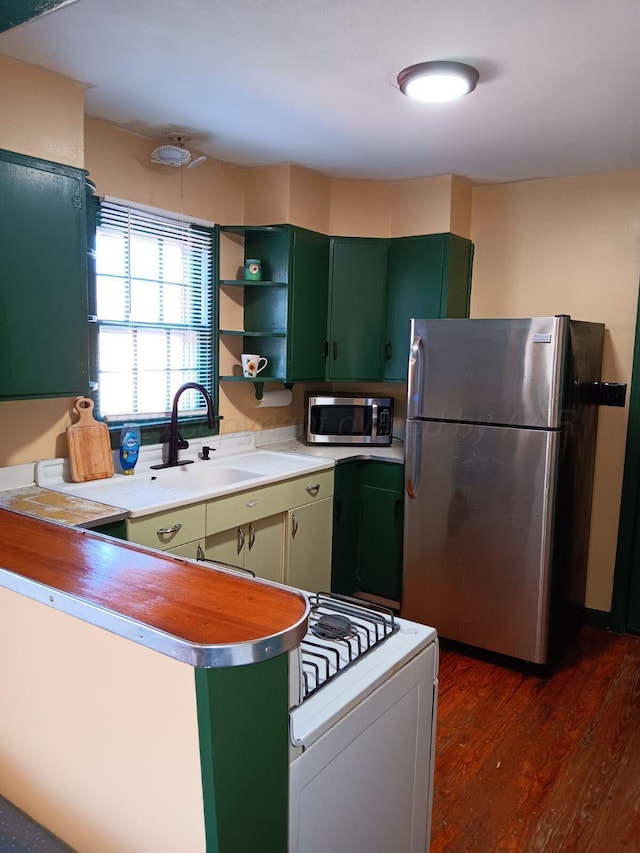 kitchen with open shelves, appliances with stainless steel finishes, dark wood-type flooring, a sink, and green cabinetry