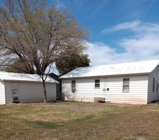 back of house featuring an outbuilding, a yard, and metal roof