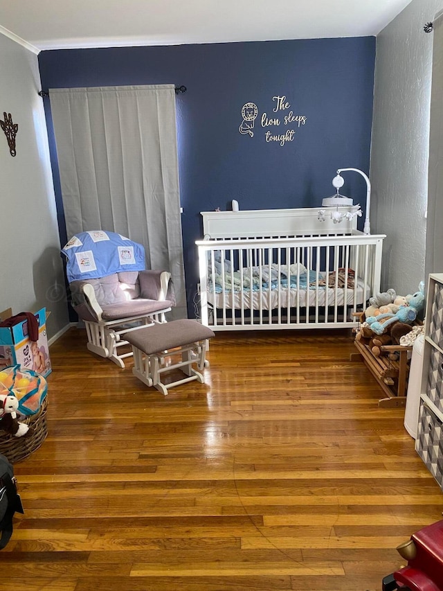 bedroom featuring a crib, hardwood / wood-style flooring, and crown molding