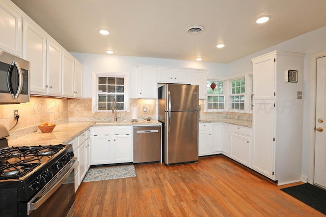 kitchen featuring wood finished floors, a sink, stainless steel appliances, white cabinets, and light stone countertops