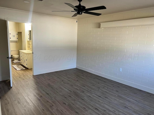 spare room featuring dark hardwood / wood-style floors, ceiling fan, crown molding, and brick wall