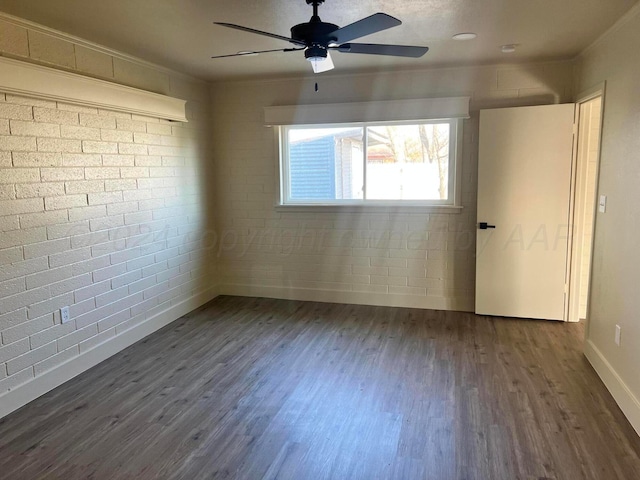 spare room featuring ornamental molding, ceiling fan, dark wood-type flooring, and brick wall